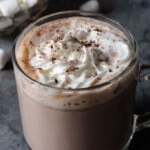 A mug of warm, slow-cooker or crockpot hot cocoa with chocolate shavings, whipped cream, and marshmallows.