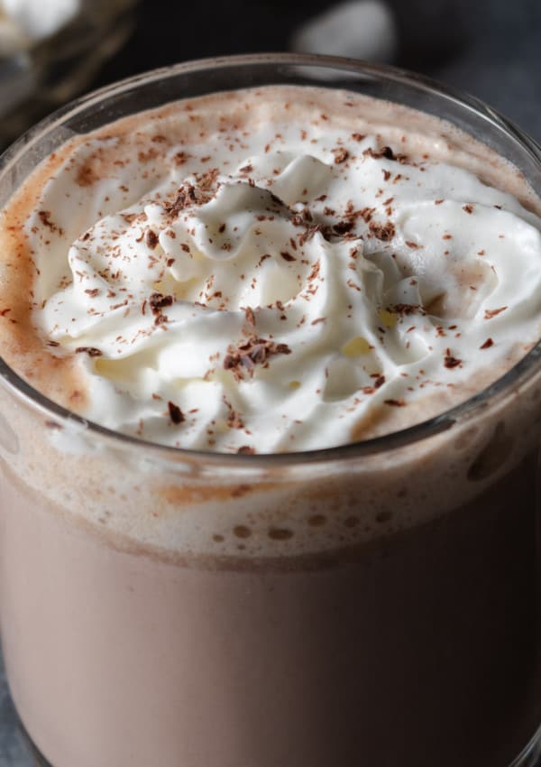 A mug of warm, slow-cooker or crockpot hot cocoa with chocolate shavings, whipped cream, and marshmallows.