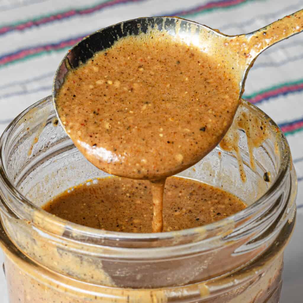 Spooning tangy lowcountry style South Carolina mustard BBQ sauce into a jar.