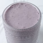 A glass with a blueberry, banana, and spinach smoothie.