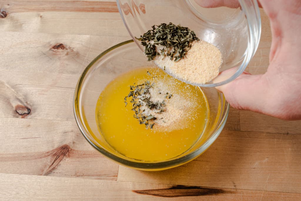 Adding a garlic herb mixture to melted butter.