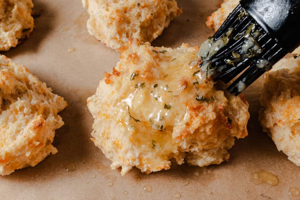 Brushing fresh cheddar bay biscuits with garlic herb butter.