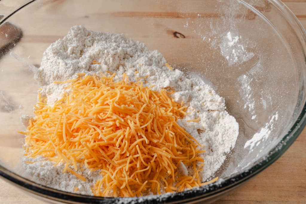 Shredded cheddar cheese added to a bowl of butter and flour.