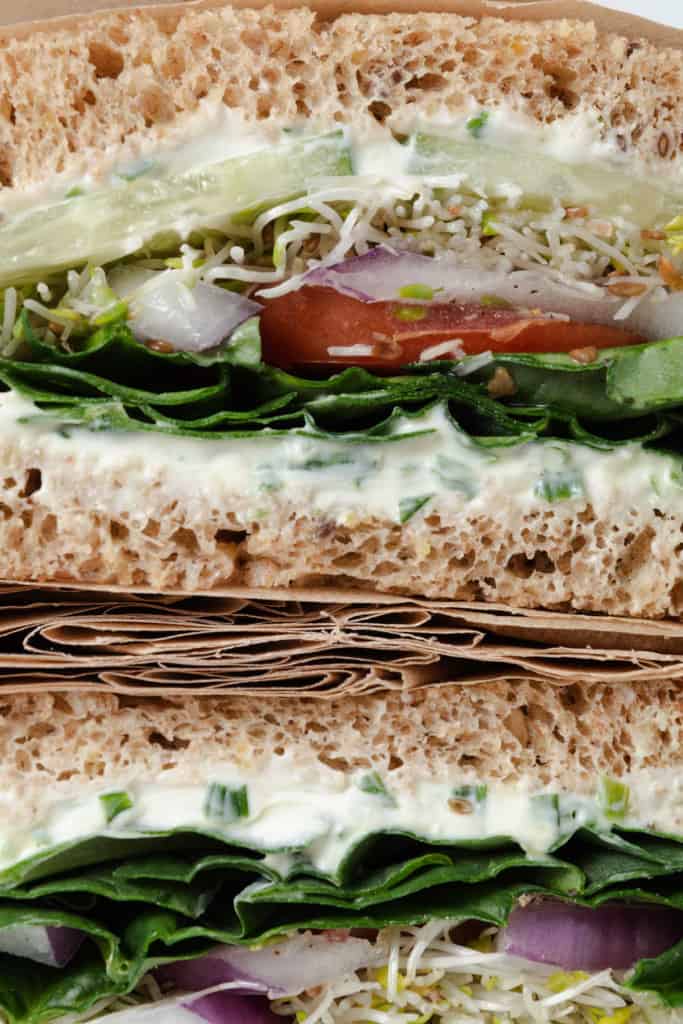 A tall sandwich made with fresh vegetables, whole grain bread, and cream cheese with chives.