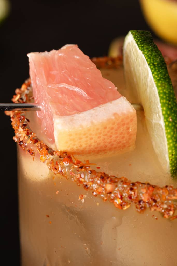 A cocktail garnished with grapefruit, lime, and spicy tajin seasoning.