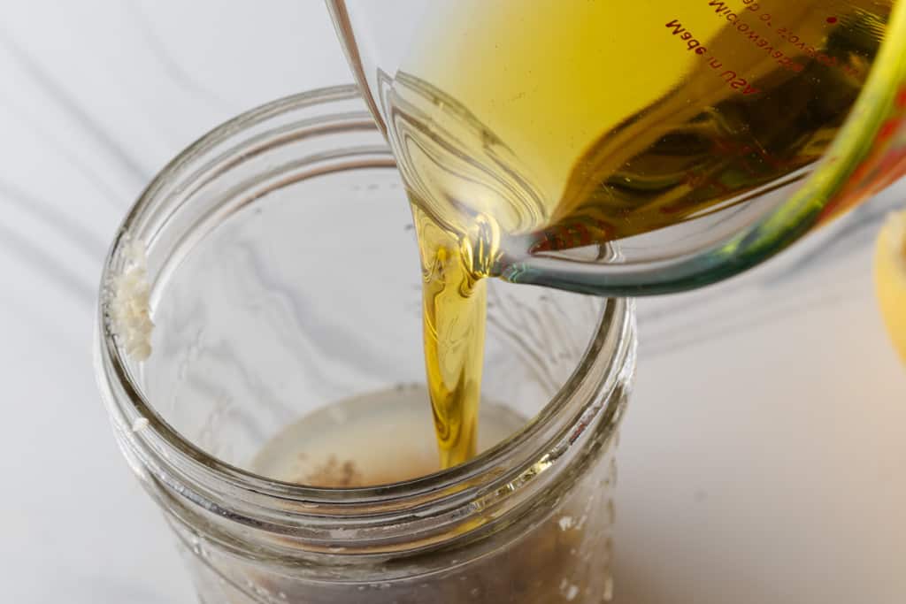 Pouring olive oil into a jar to make lemon vinaigrette.