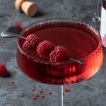 A valentine red love potion cocktail garnished with fresh raspberries and hearts.
