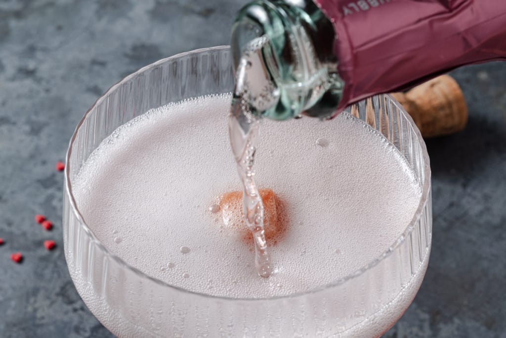 Pouring pink champagne over a sugar cube and bitters.