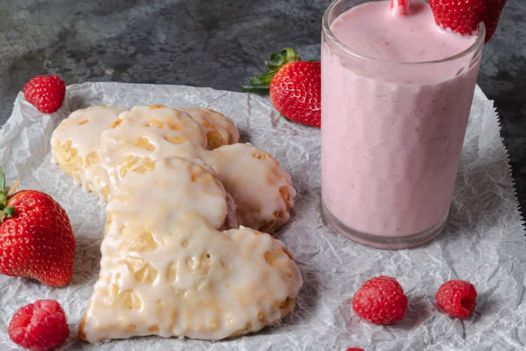A pink and red Valentine's Day breakfast with heart-shaped strawberry pastries, a pink smoothie, strawberries, and raspberries.