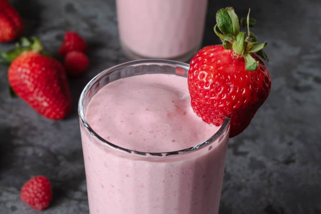 A pink smoothie in a glass with raspberries and strawberries.