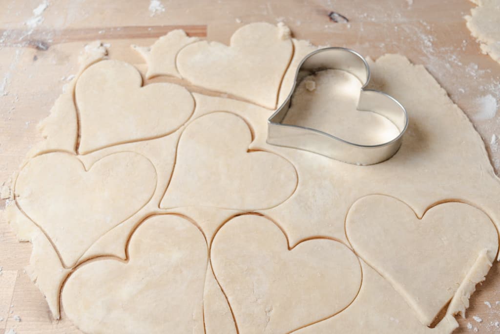 A rolled-out piece of pie dough with heart shapes cut out.