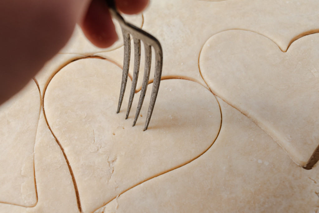 Pricking heart-shaped pie dough with a fork.