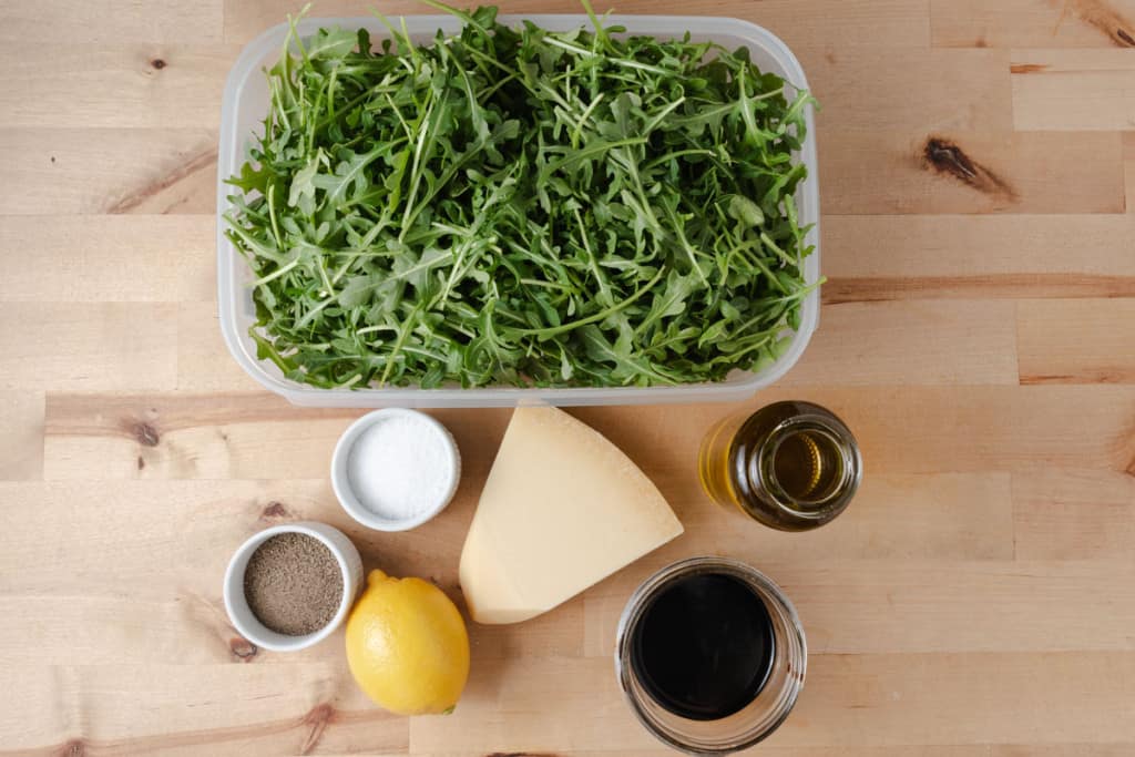 Baby arugula, balsamic glaze, extra virgin olive oil, salt, pepper, a lemon, and a wedge of parmesan cheese.