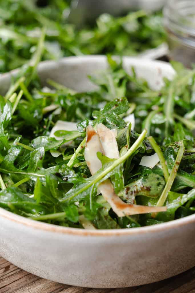 A bowl of arugula salad with lemon, parmesan, olive oil, and balsamic vinegar glaze.