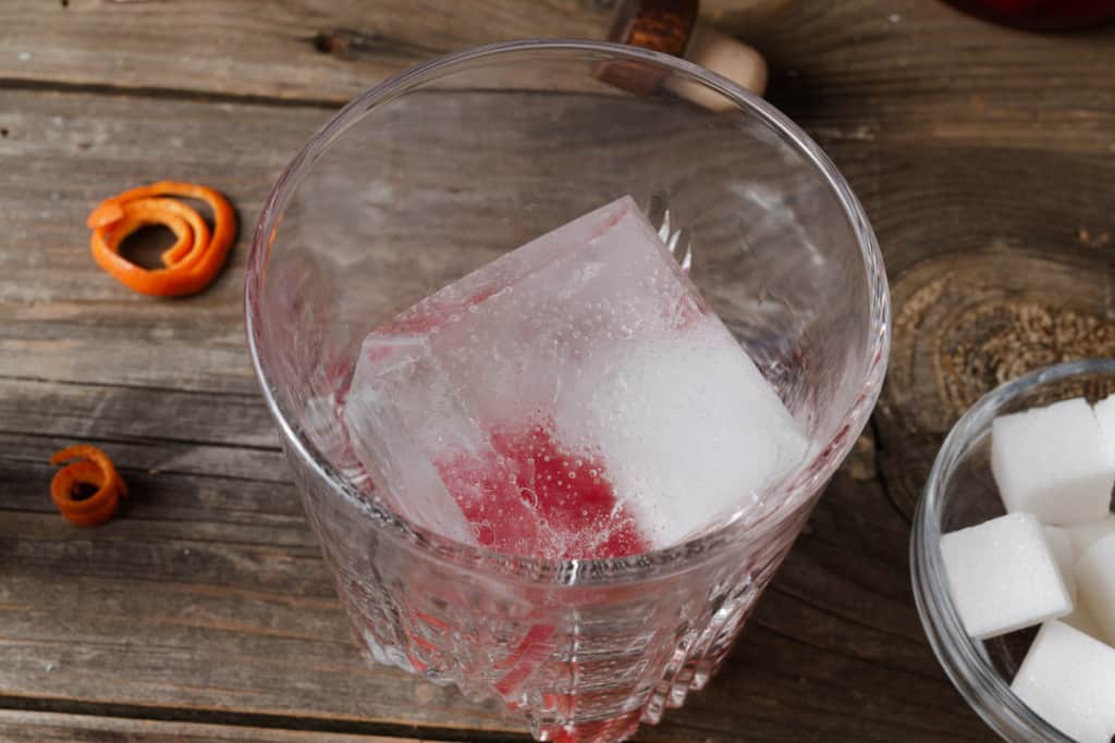 Adding a large chunk of ice to a rocks glass.