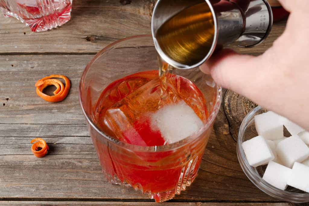 Pouring black cherry whiskey into a rocks glass.