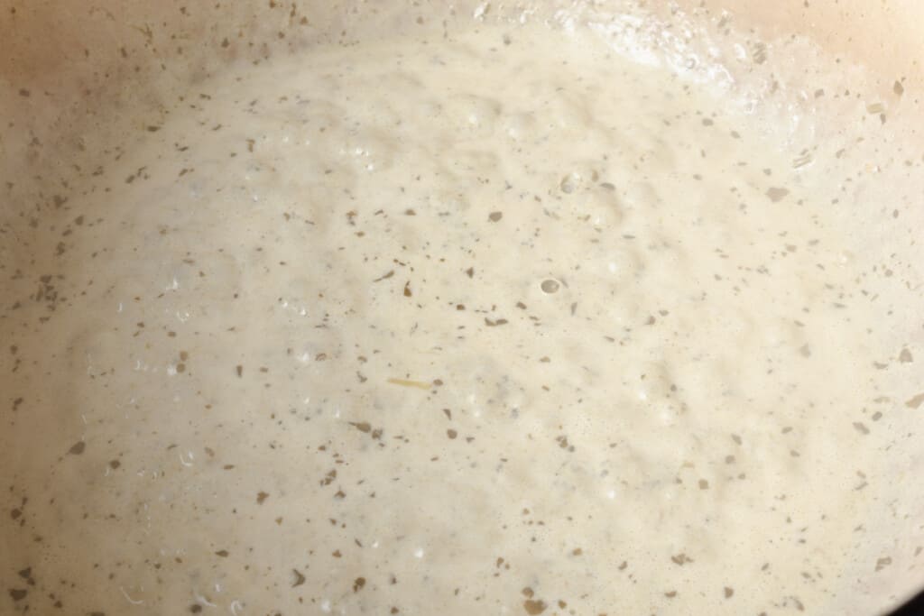 Simmering pesto cream sauce in a pot.