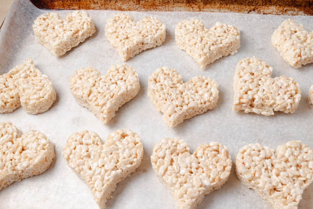 Heart-shaped rice krispies treats on a parchment lined baking sheet.