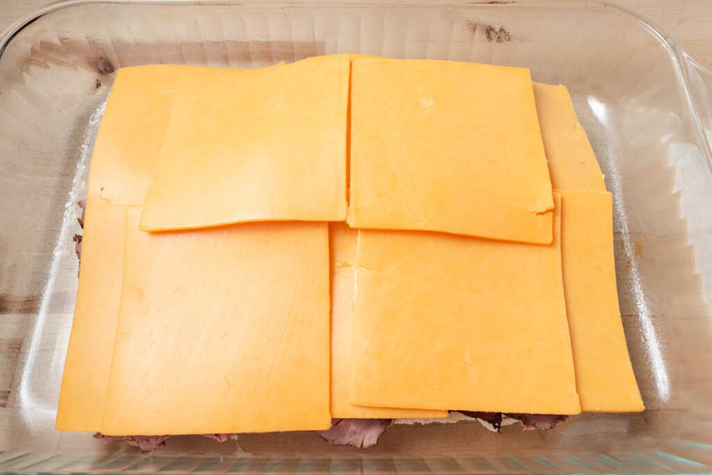 Adding a layer of cheese to mini sandwiches.