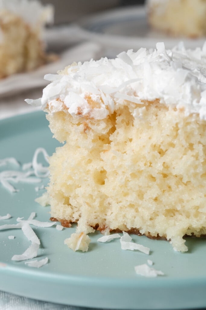 A slice of coconut poke cake with cream of coconut, cool whip, and shredded coconut.