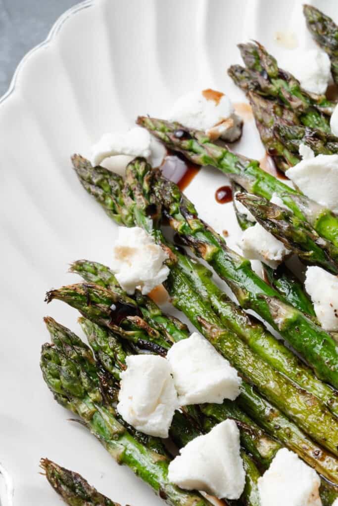 A platter of grilled asparagus with balsamic glaze and crumbled goat cheese.