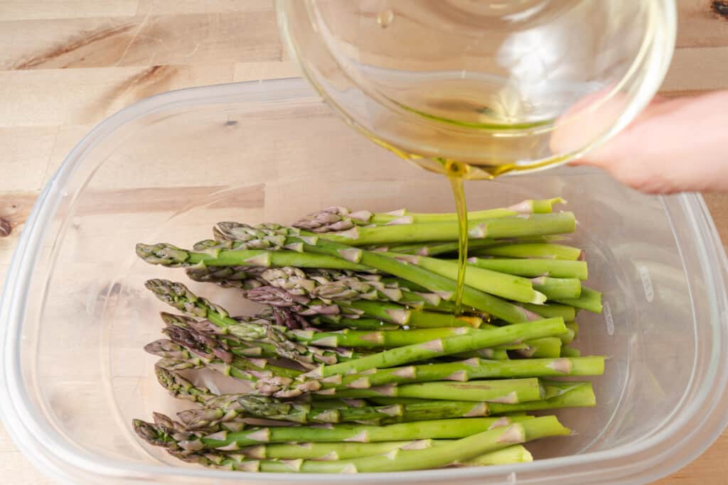 Pouring olive oil over asparagus.