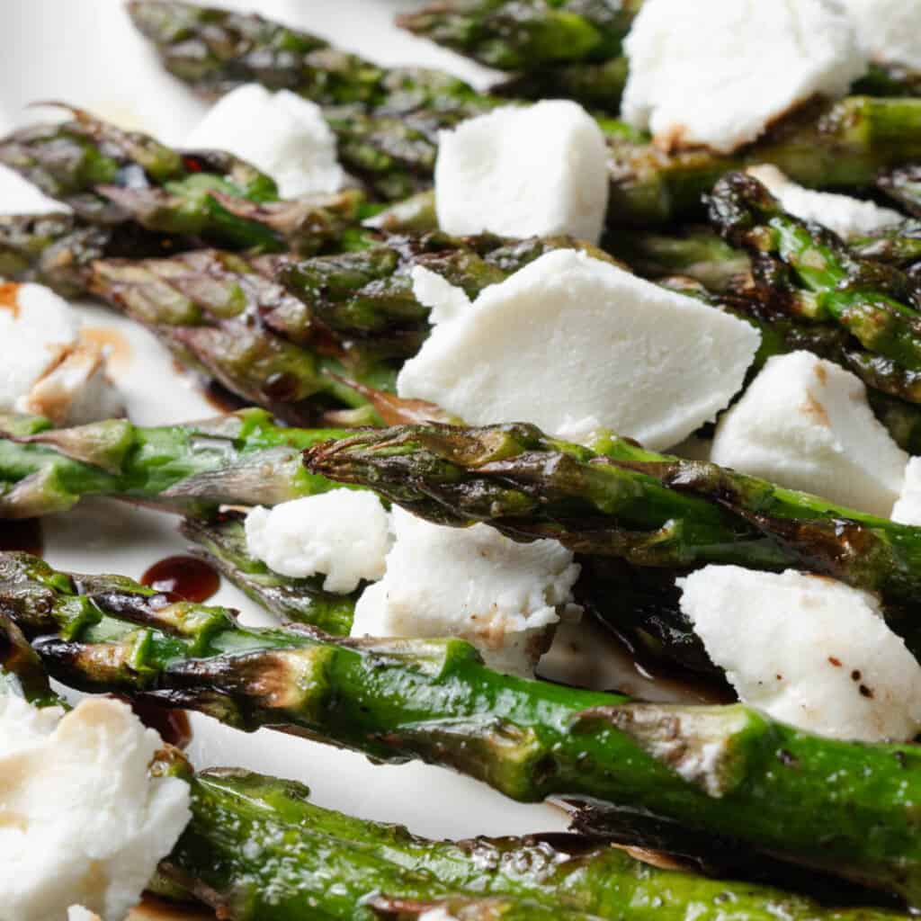 A platter of grilled asparagus with balsamic glaze and crumbled goat cheese.