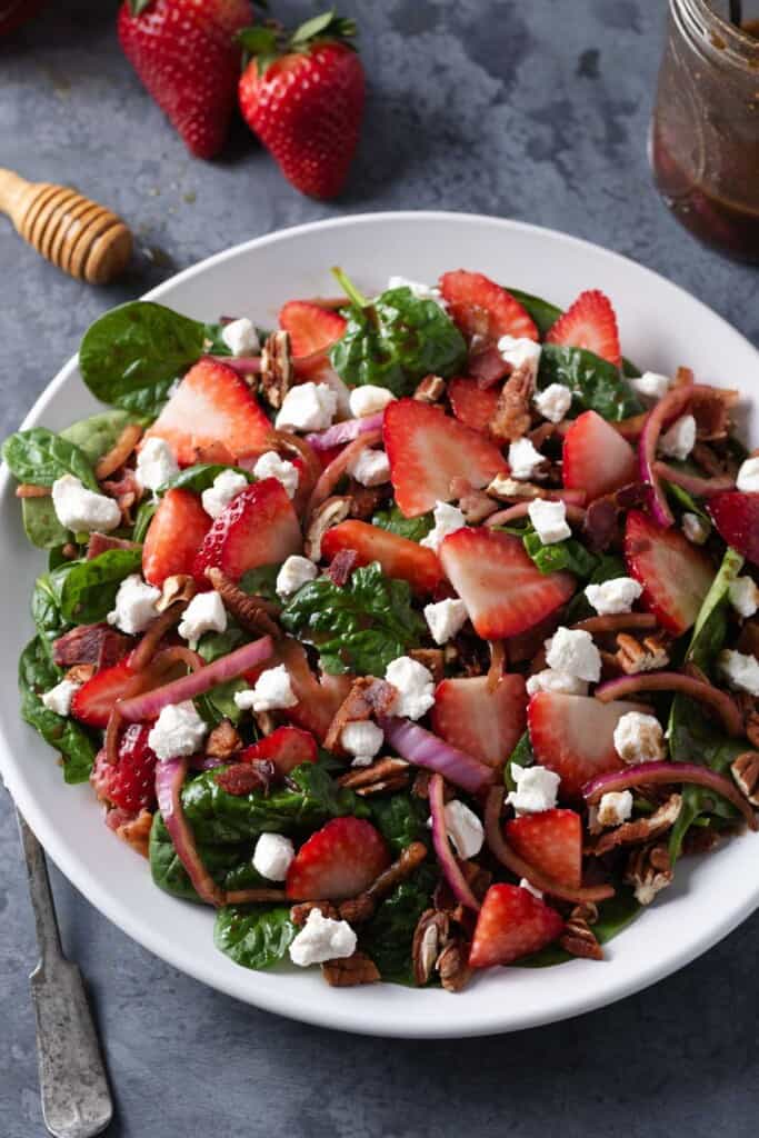 Summer strawberry, goat cheese, and spinach salad on a white plate.