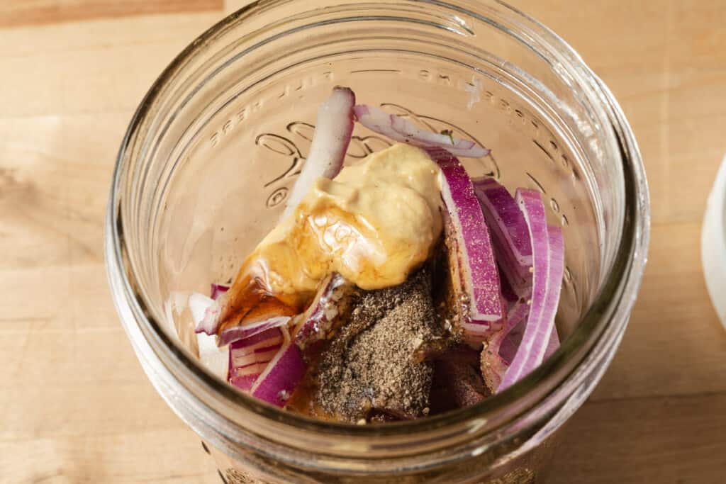 Balsamic vinaigrette ingredients and sliced red onions in a mason jar.