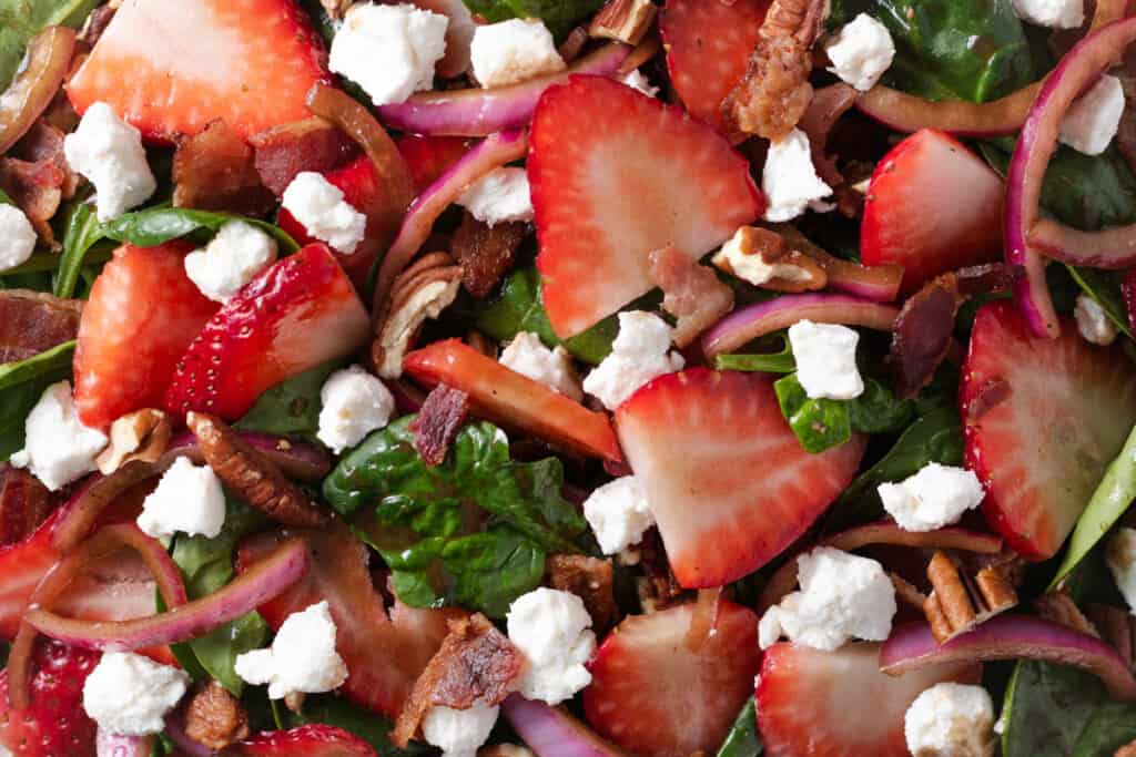 A salad with spinach, strawberries, goat cheese, pecans, onions, and bacon.