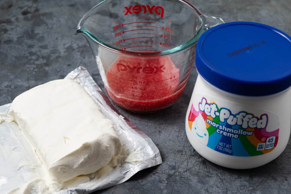 A block of cream cheese, a jar of marshmallow creme, and a cup of homemade strawberry puree.