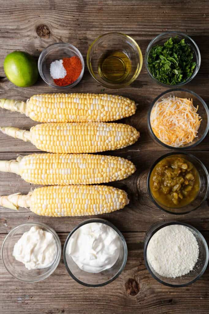 Corn on the cob, cilantro, paprika, cayenne pepper, Cotija, shredded cheese, sour cream, mayonnaise, green chilis, oil, and lime mise en place ready to make corn dip.