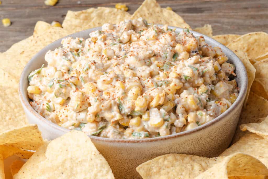 A bowl of Mexican street corn dip with tortilla chips.