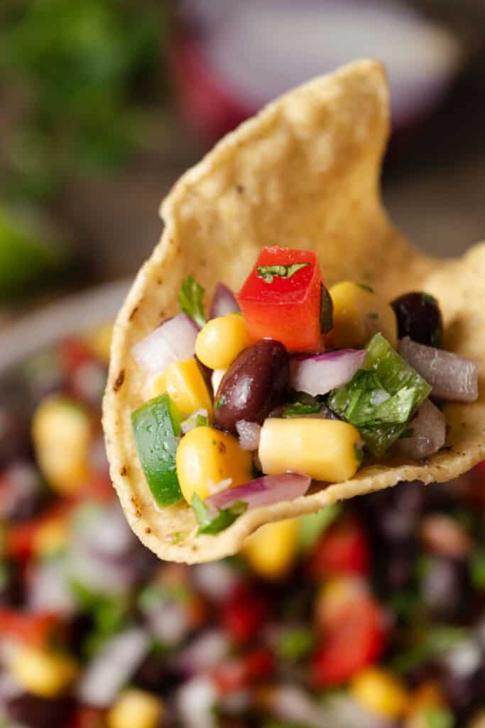 A tortilla chip with black bean and corn salsa on it.