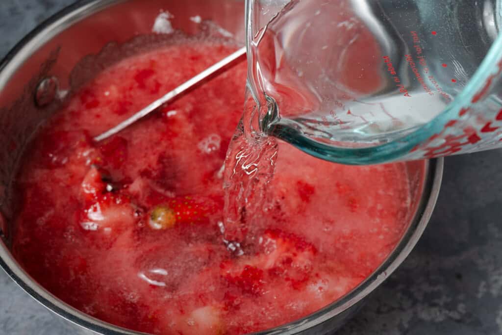 Adding water to mashed strawberries and sugar.