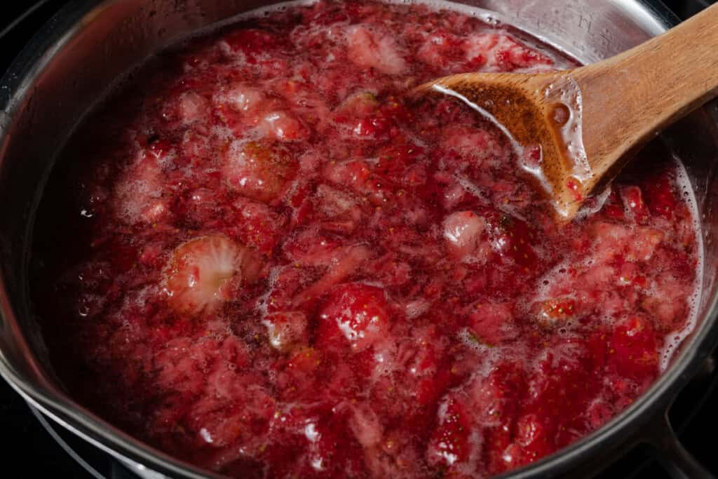 Heating crushed strawberries and water in a pot.