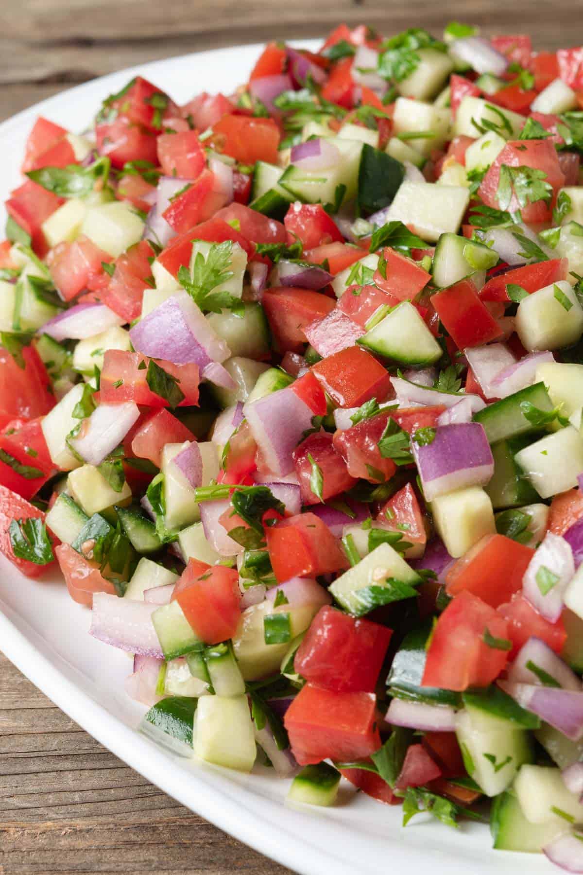 A white platter of Mediterranean tomato and cucumber salad.
