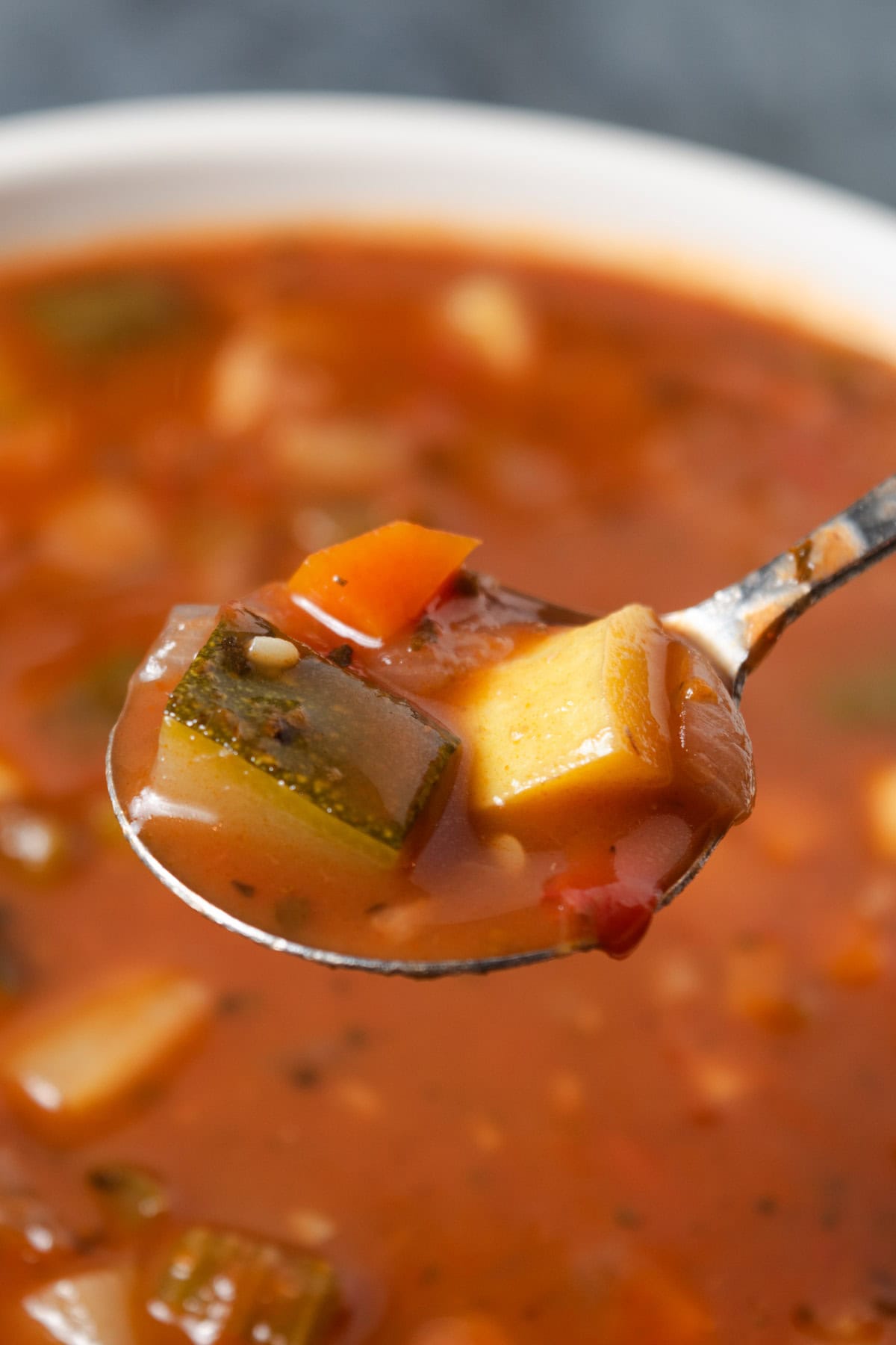 A spoonful of summer vegetable soup with zucchini, yellow squash, and red wine.