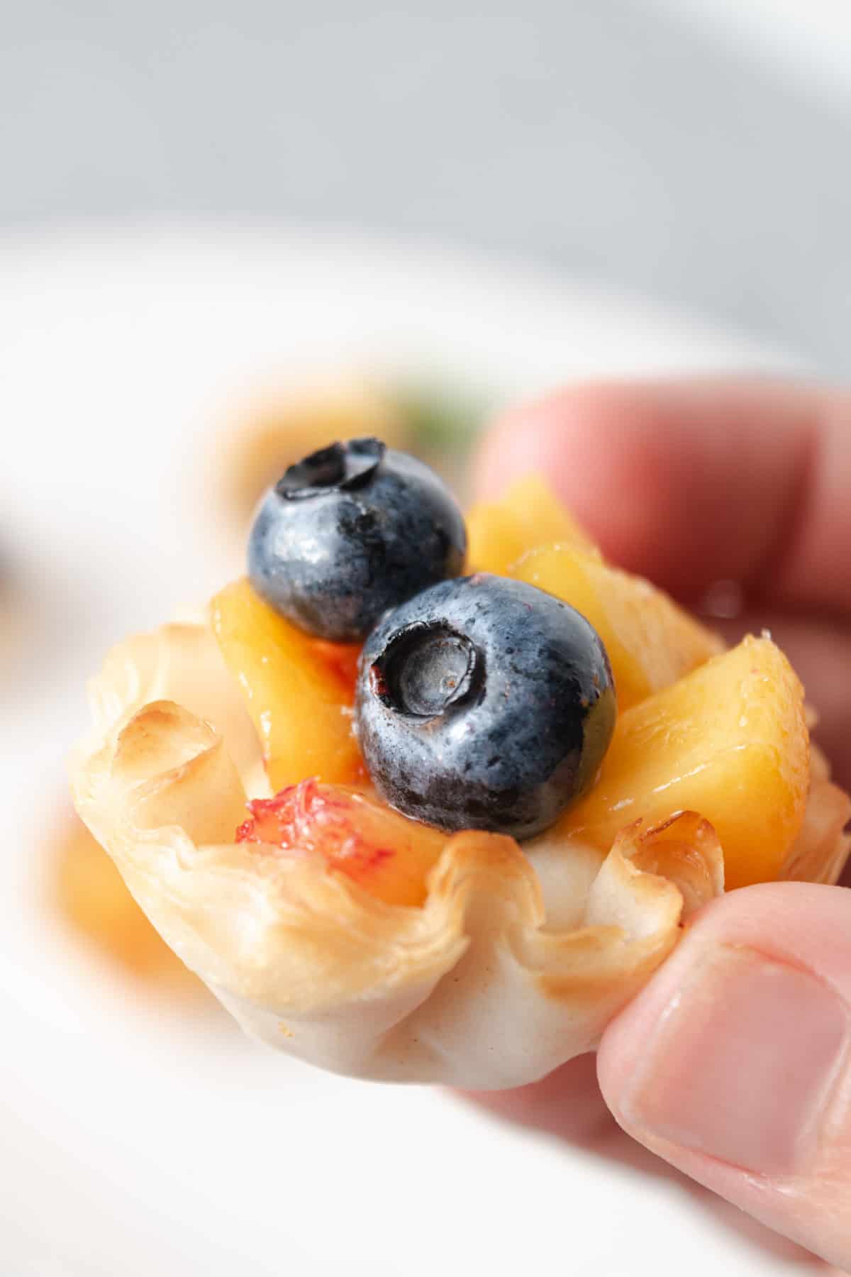 A bite sized phyllo peach and blueberry tart filled with mascarpone cream.