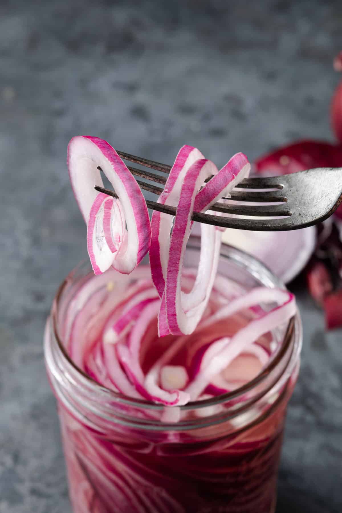 Using a fork to pick up rings of homemade pickled red onions out of a jar.