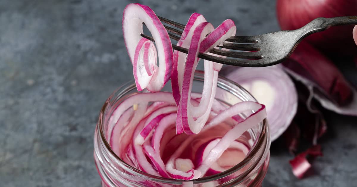 Picking pickled red onions up from a jar with a fork.