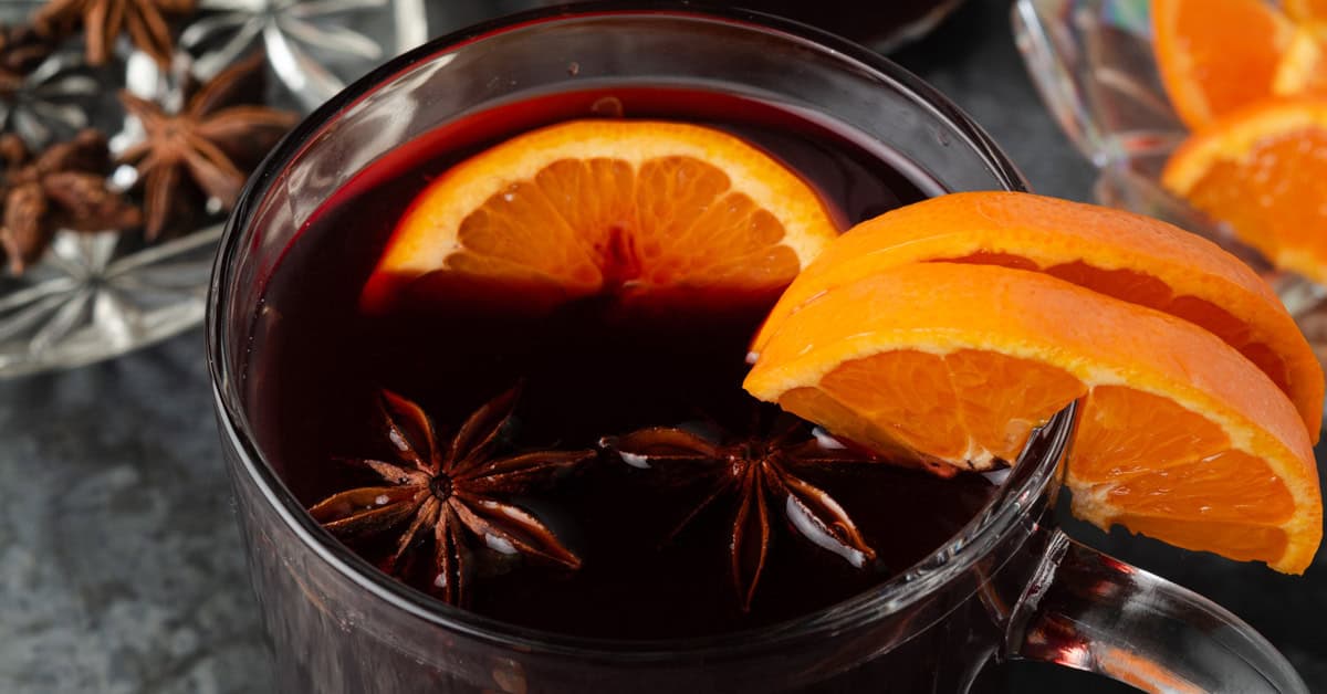 A glass mug of mulled red wine with orange slices and star anise.