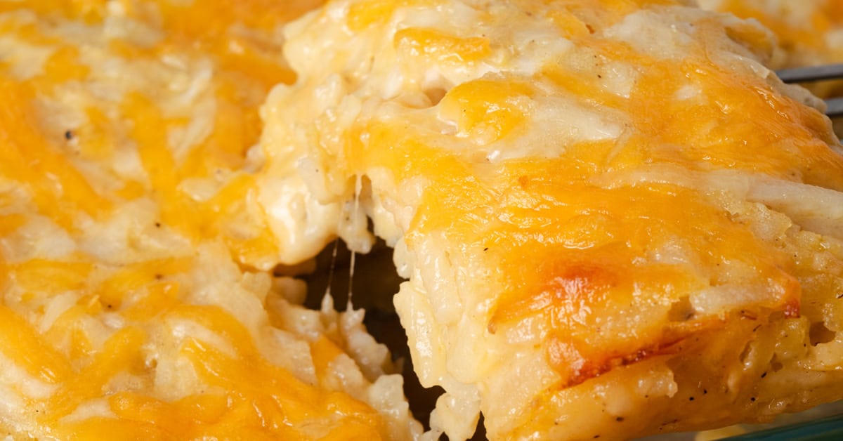 Removing a slice of cheesy hashbrown casserole from a baking dish.