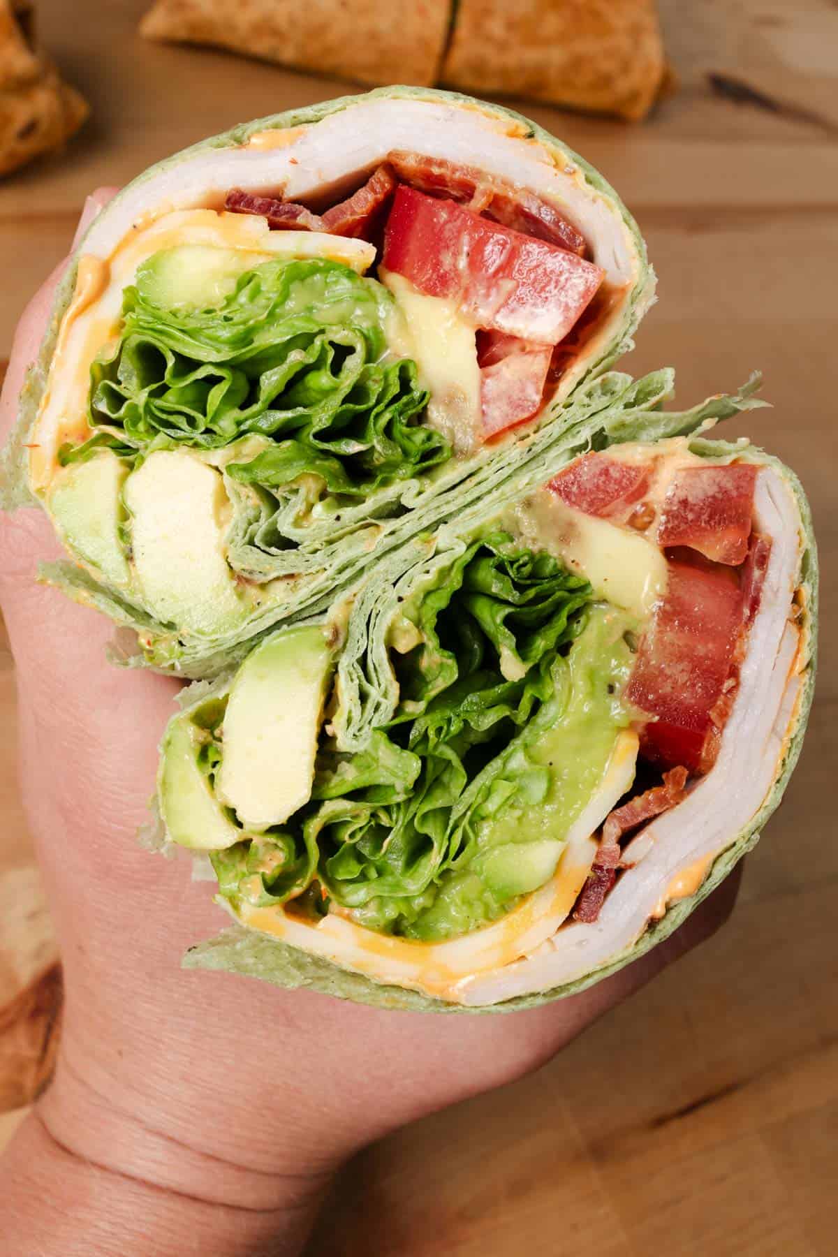 A hand holding a turkey wrap cut in half.