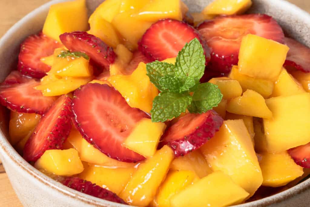 Strawberries, mango, honey, and lime in a bowl.