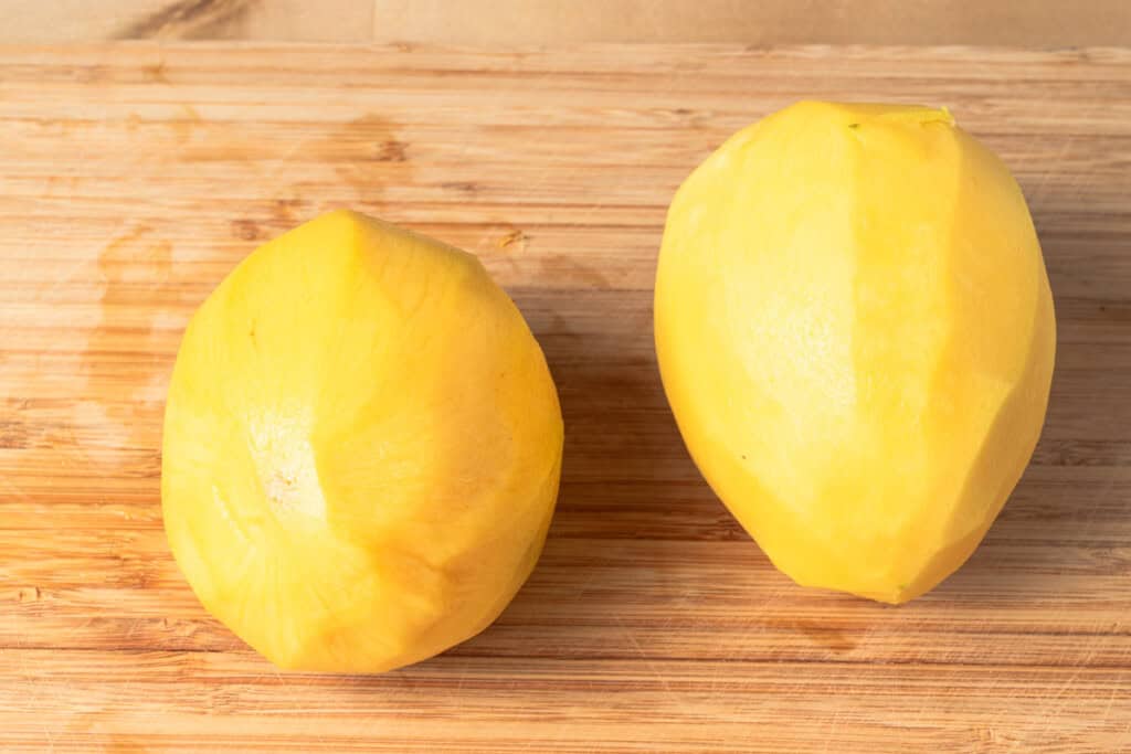 Two peeled mangoes on a cutting board.