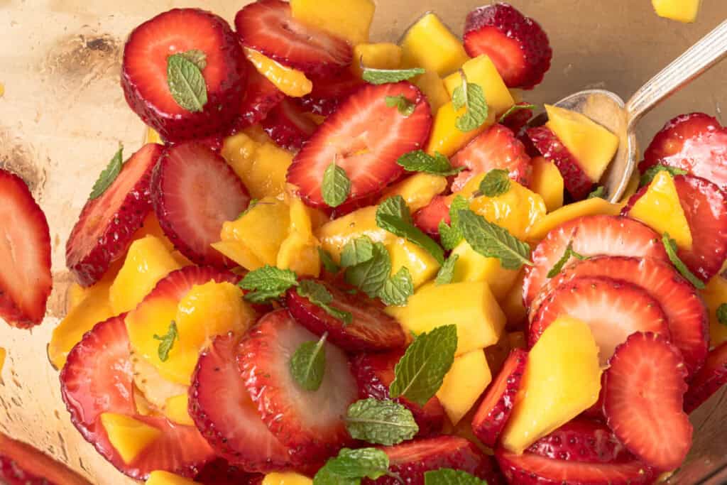 Strawberries, mango, honey, lime, and mint in a bowl.