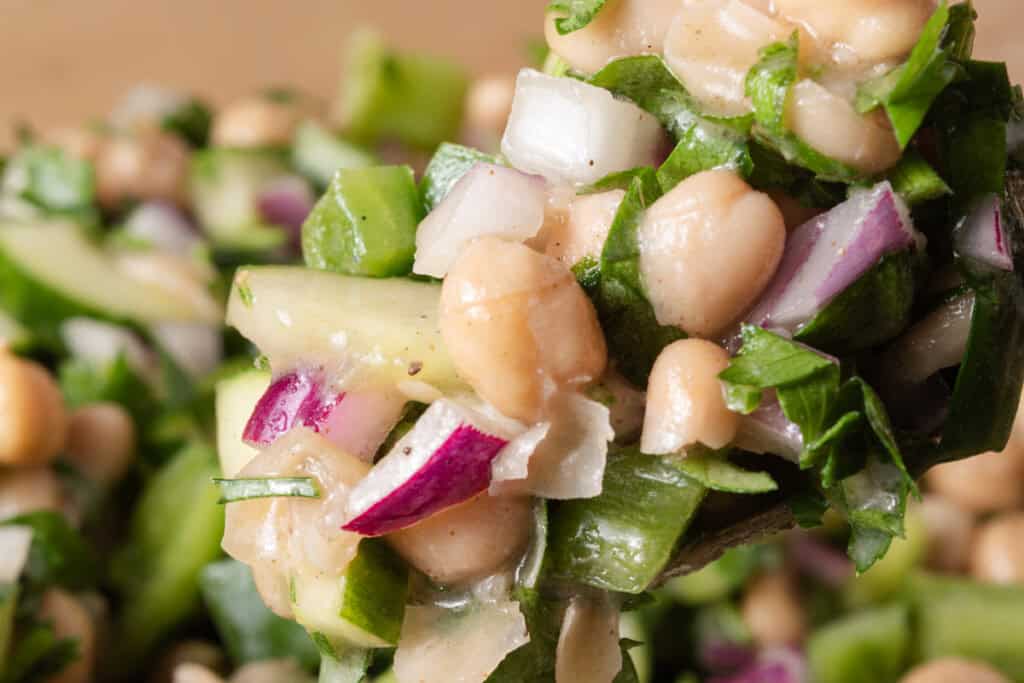 A spoonful of fresh white bean, chickpea ,and cucumber salad with bell peppers, onions, and parsley.
