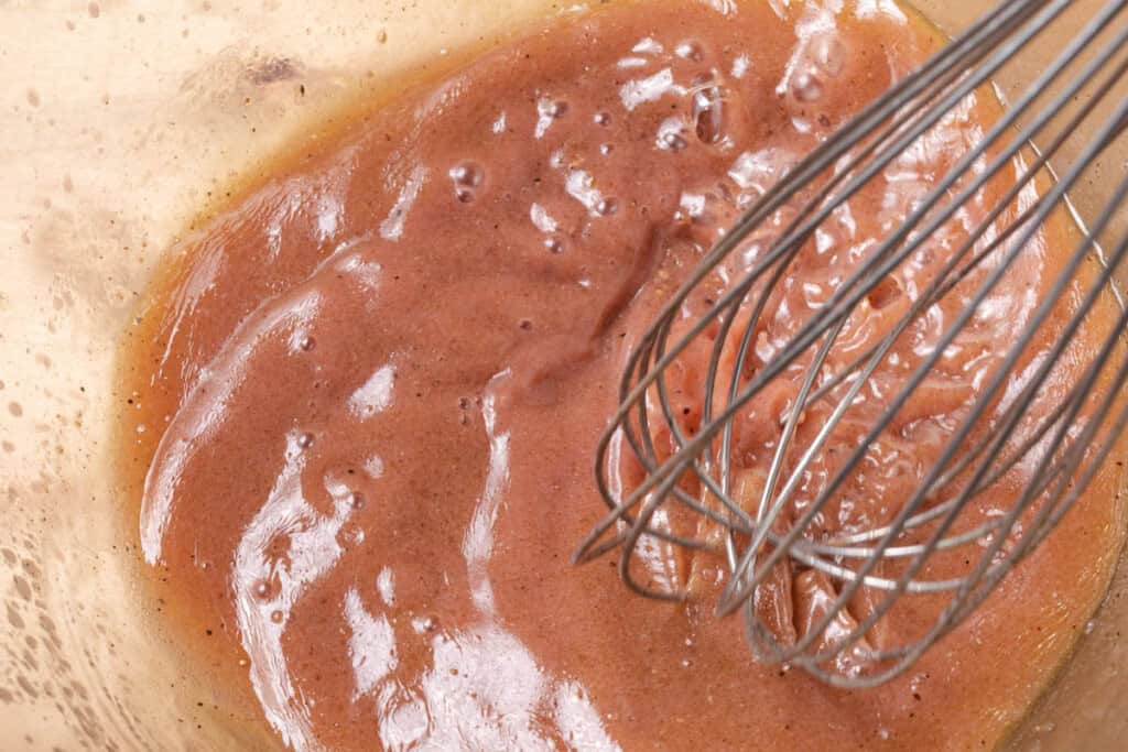 Whisking red wine vinegar, extra virgin olive oil, and Dijon mustard in a bowl to make a vinaigrette.