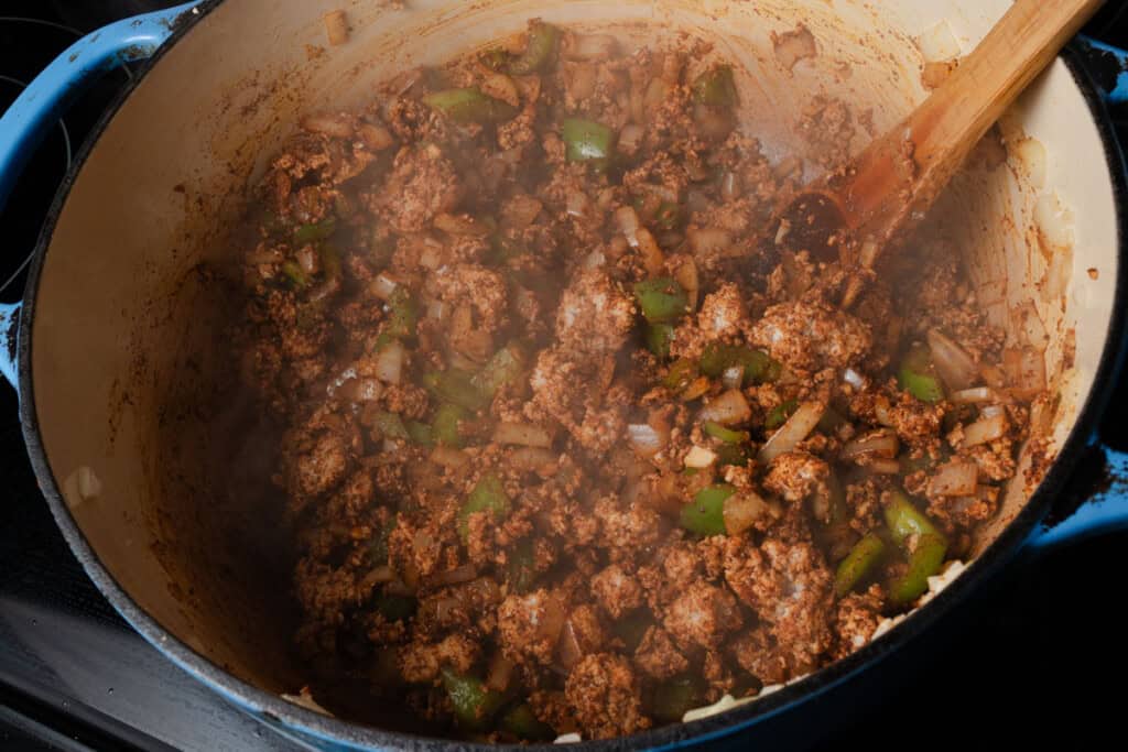 Stirring peppers, onions, garlic, ground turkey, and chili spices in a dutch oven.